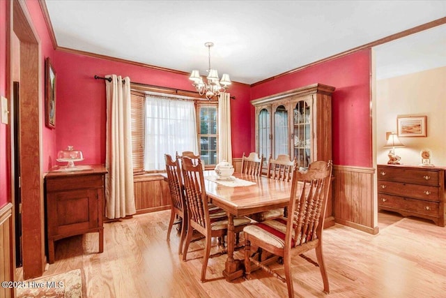 dining area featuring a notable chandelier, wooden walls, ornamental molding, and light wood-type flooring