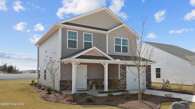 view of front of home featuring a porch, concrete driveway, a front lawn, and stone siding