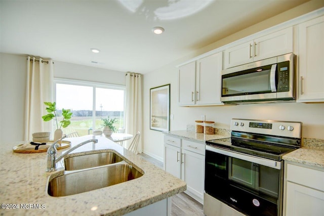 kitchen featuring appliances with stainless steel finishes, sink, white cabinets, light stone counters, and light hardwood / wood-style floors