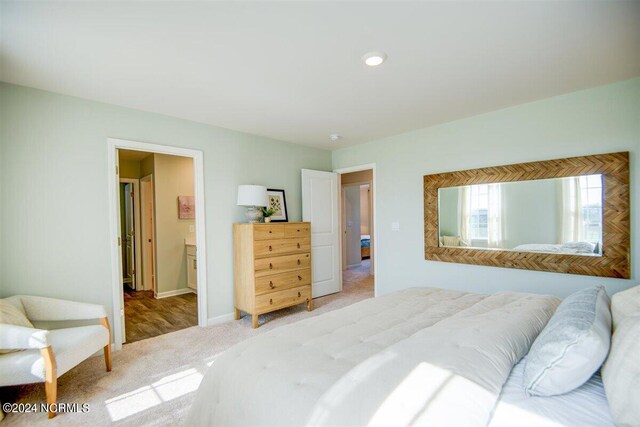 bedroom with baseboards, connected bathroom, and light colored carpet