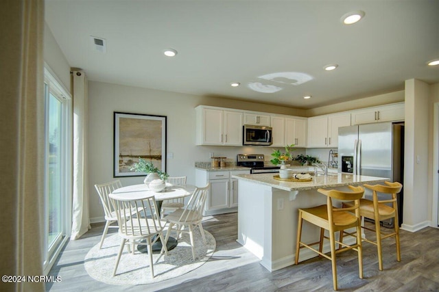 kitchen featuring white cabinetry, appliances with stainless steel finishes, a kitchen island with sink, and light hardwood / wood-style floors