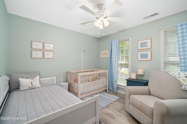 bedroom featuring a crib, ceiling fan, and light hardwood / wood-style floors