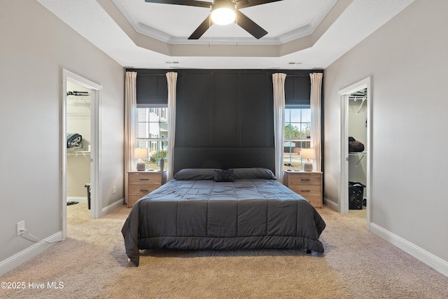 bedroom featuring light carpet, a tray ceiling, and a walk in closet