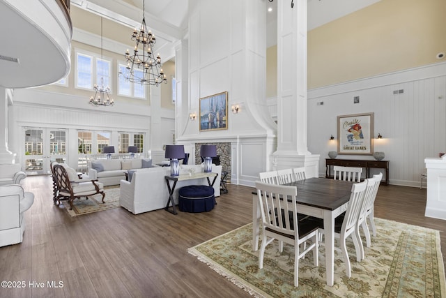 dining area with a chandelier, hardwood / wood-style floors, beam ceiling, decorative columns, and a high ceiling