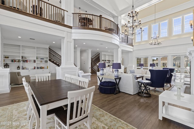 dining area with a notable chandelier, dark wood-type flooring, a high ceiling, and ornate columns