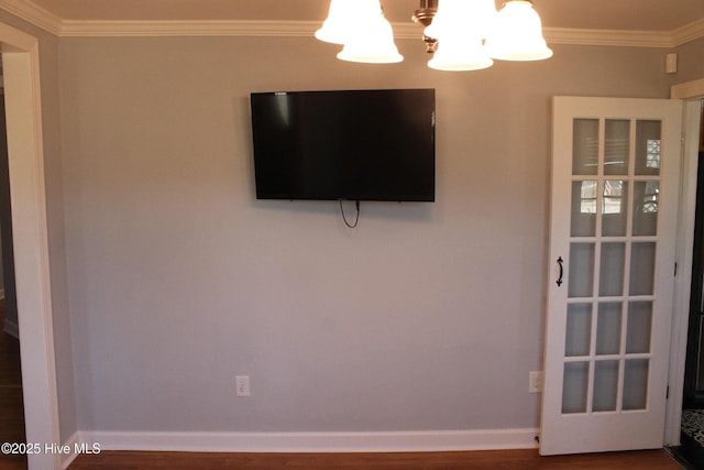 empty room featuring wood-type flooring, ornamental molding, and a chandelier