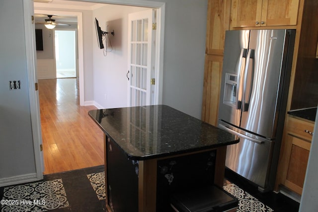 kitchen with dark wood-type flooring, a center island, stainless steel fridge, ceiling fan, and dark stone counters