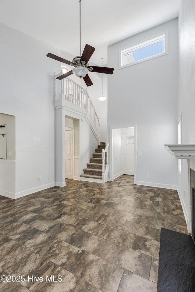 unfurnished living room with stone finish flooring, ceiling fan, a fireplace, a high ceiling, and stairs