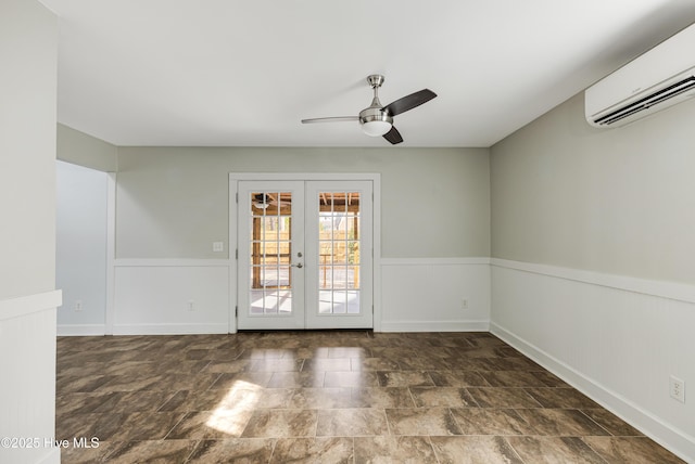 unfurnished room featuring stone finish floor, ceiling fan, an AC wall unit, french doors, and wainscoting
