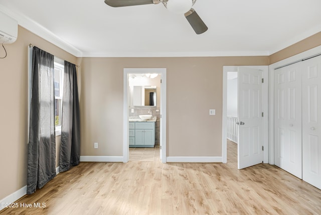 unfurnished bedroom with light wood finished floors, a sink, a wall mounted air conditioner, crown molding, and baseboards