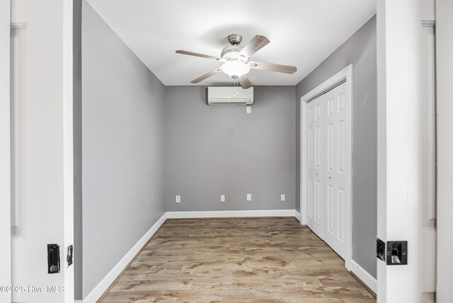 unfurnished bedroom featuring a closet, ceiling fan, light wood-type flooring, baseboards, and an AC wall unit