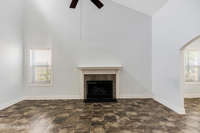 unfurnished living room featuring a fireplace, high vaulted ceiling, a ceiling fan, baseboards, and arched walkways