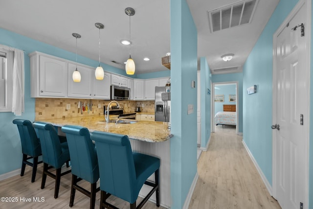 kitchen featuring a breakfast bar area, white cabinetry, hanging light fixtures, stainless steel appliances, and kitchen peninsula