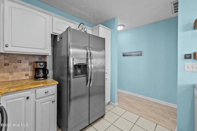 kitchen with tasteful backsplash, white cabinetry, stainless steel fridge, light tile patterned floors, and a textured ceiling