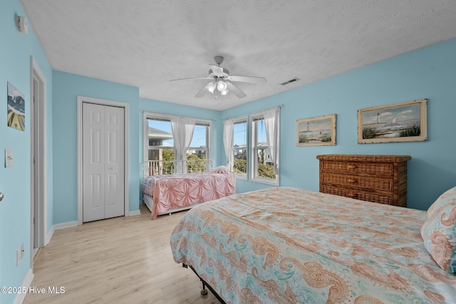 bedroom with a closet, ceiling fan, light hardwood / wood-style floors, and a textured ceiling