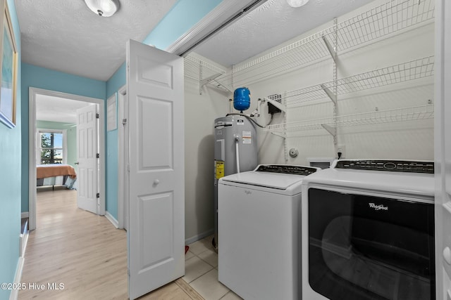 clothes washing area with light wood-type flooring, electric water heater, washer and dryer, and a textured ceiling