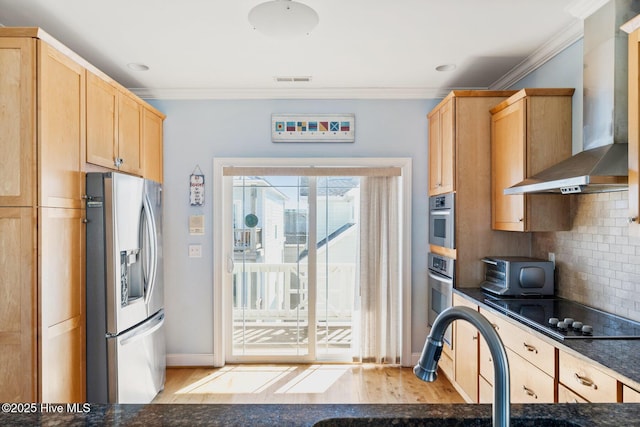 kitchen with wall chimney exhaust hood, crown molding, light brown cabinets, appliances with stainless steel finishes, and decorative backsplash