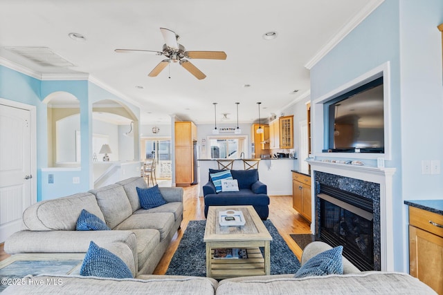 living room with crown molding, a high end fireplace, ceiling fan, and light wood-type flooring