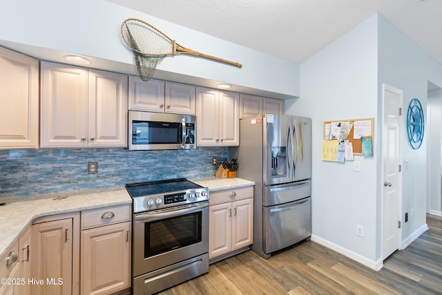 kitchen with a textured ceiling, light wood-style flooring, stainless steel appliances, baseboards, and backsplash