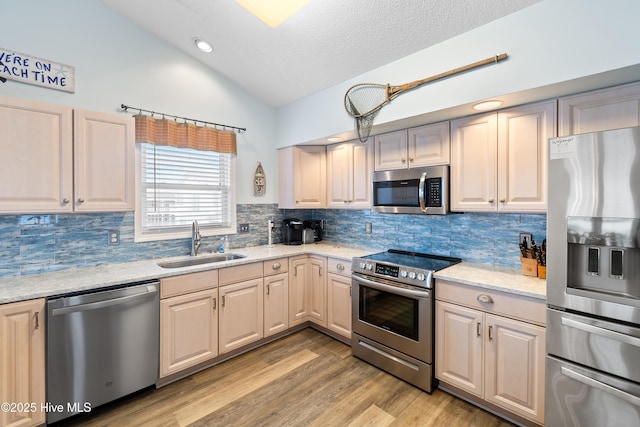 kitchen with stainless steel appliances, decorative backsplash, vaulted ceiling, a sink, and light wood-type flooring