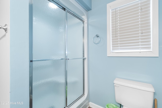 full bathroom featuring a shower with shower door and toilet