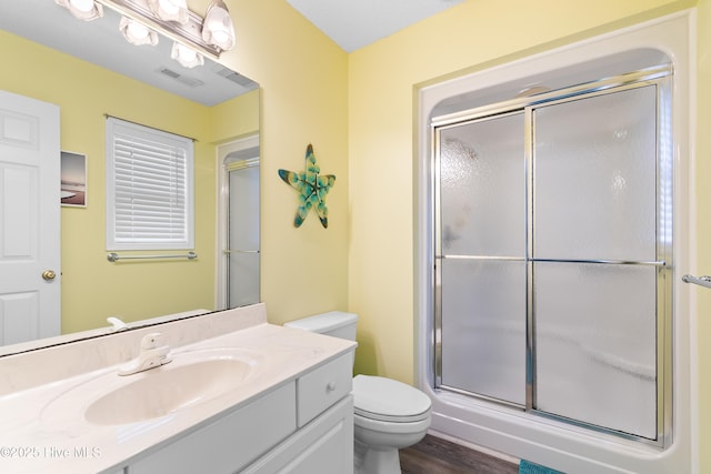 bathroom featuring visible vents, toilet, a shower with shower door, vanity, and wood finished floors