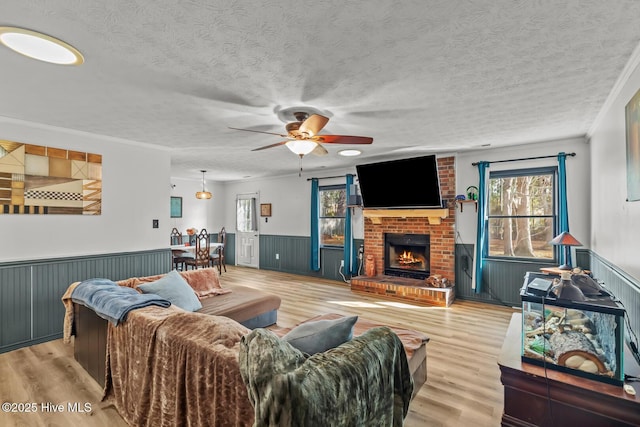 living room with ornamental molding, light hardwood / wood-style floors, a brick fireplace, and a textured ceiling