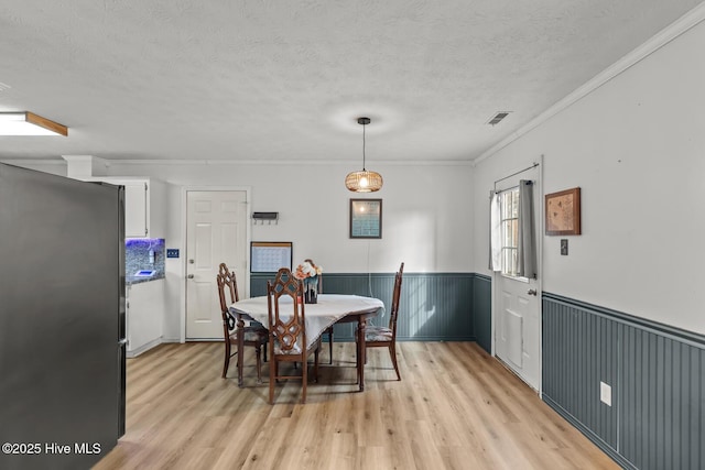 dining room with crown molding, light wood-type flooring, and a textured ceiling