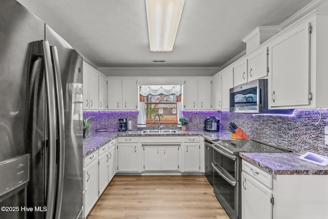 kitchen with sink, light wood-type flooring, appliances with stainless steel finishes, decorative backsplash, and white cabinets