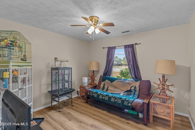 living area with wood-type flooring, a textured ceiling, and ceiling fan