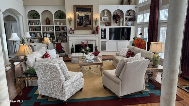 living room with built in shelves, a fireplace, wood-type flooring, and ornate columns