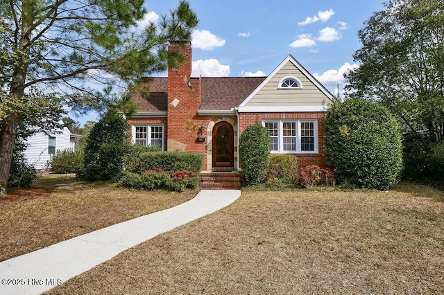 view of front of property featuring a shingled roof, a chimney, a front lawn, and brick siding