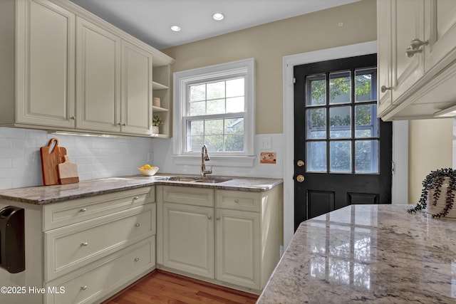 kitchen featuring light stone countertops, recessed lighting, a sink, light wood-style floors, and decorative backsplash