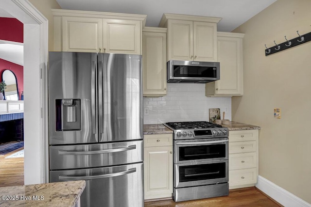 kitchen with light stone counters, cream cabinetry, stainless steel appliances, decorative backsplash, and wood finished floors