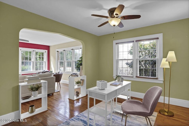 office space featuring a ceiling fan, baseboards, arched walkways, and hardwood / wood-style floors