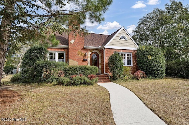 view of front of house with a shingled roof, a front lawn, and brick siding