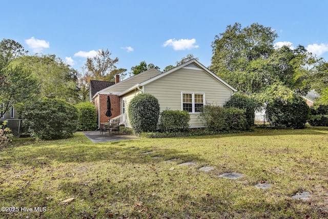 view of property exterior with brick siding, a chimney, a lawn, and a patio