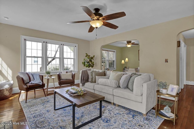 living area featuring a ceiling fan, arched walkways, baseboards, and hardwood / wood-style flooring