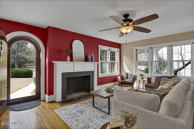 living room with ceiling fan, light wood-type flooring, a fireplace, and a healthy amount of sunlight