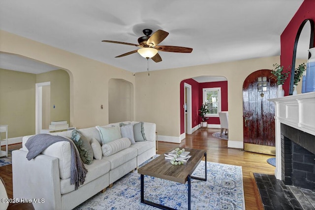 living room featuring a fireplace with flush hearth, arched walkways, baseboards, and wood finished floors