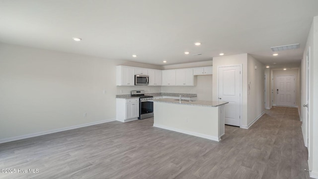 kitchen with light hardwood / wood-style flooring, appliances with stainless steel finishes, white cabinetry, light stone counters, and a center island with sink