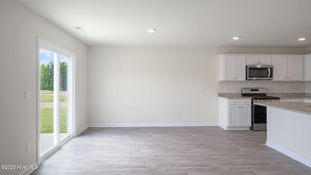 kitchen featuring light stone counters, appliances with stainless steel finishes, light hardwood / wood-style floors, and white cabinets