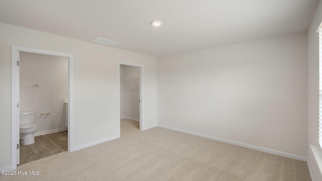 unfurnished bedroom featuring light carpet, a walk in closet, a closet, and ensuite bath