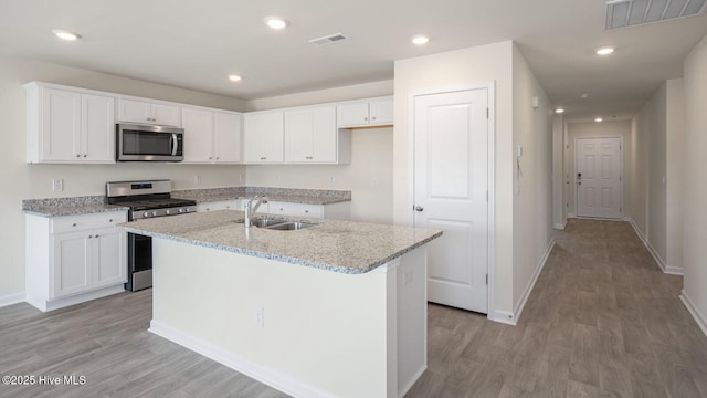 kitchen with an island with sink, sink, white cabinets, light stone counters, and stainless steel appliances