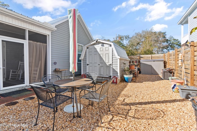 view of patio featuring an outbuilding, a storage unit, a fenced backyard, and outdoor dining area