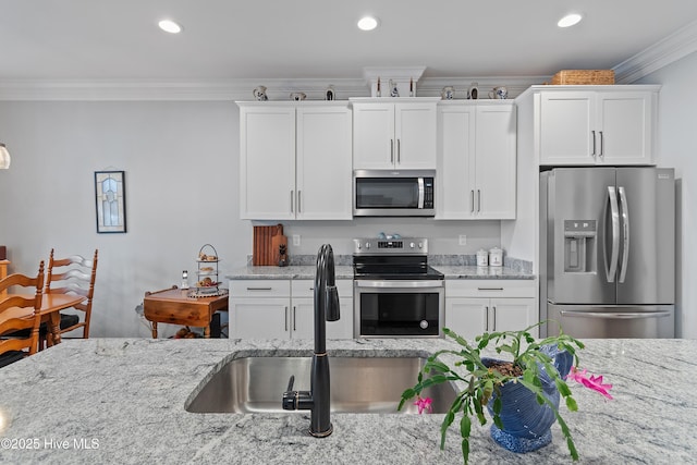 kitchen with a sink, white cabinetry, stainless steel appliances, crown molding, and light stone countertops