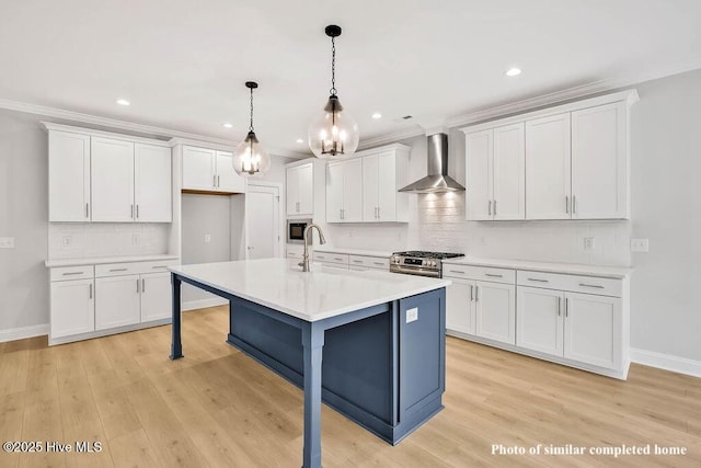 kitchen with wall chimney exhaust hood, appliances with stainless steel finishes, a sink, and white cabinetry