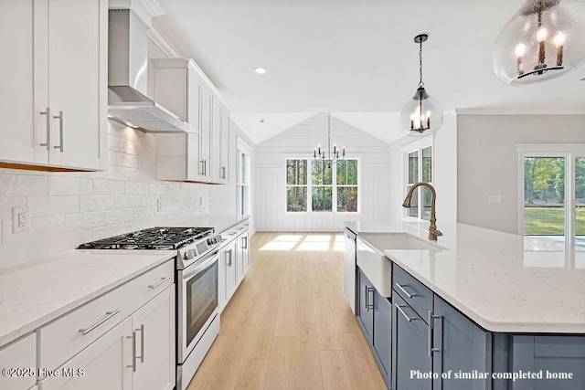 kitchen featuring white cabinets, a sink, stainless steel appliances, wall chimney range hood, and a notable chandelier