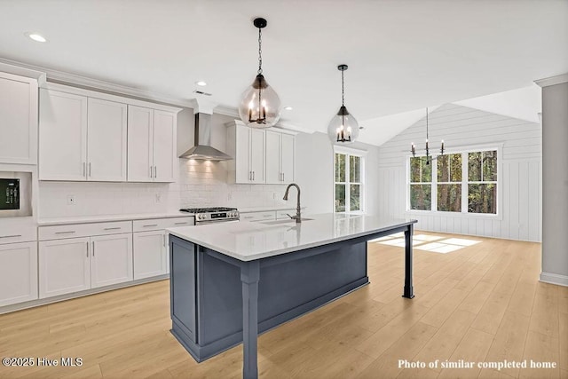 kitchen featuring light countertops, decorative backsplash, a kitchen island with sink, a sink, and wall chimney exhaust hood