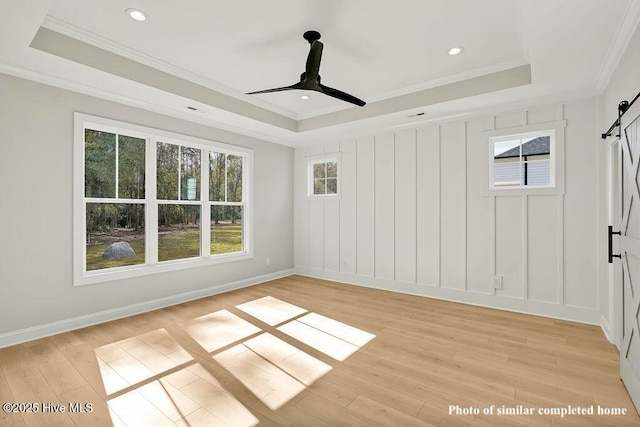 interior space featuring light wood-style floors, a barn door, a tray ceiling, and crown molding